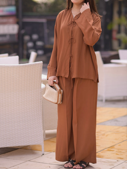 Woman in a brown outfit holding a beige clutch outdoors.