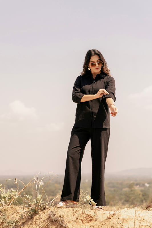 Person wearing a black outfit standing on a rocky landscape with a cloudy sky.