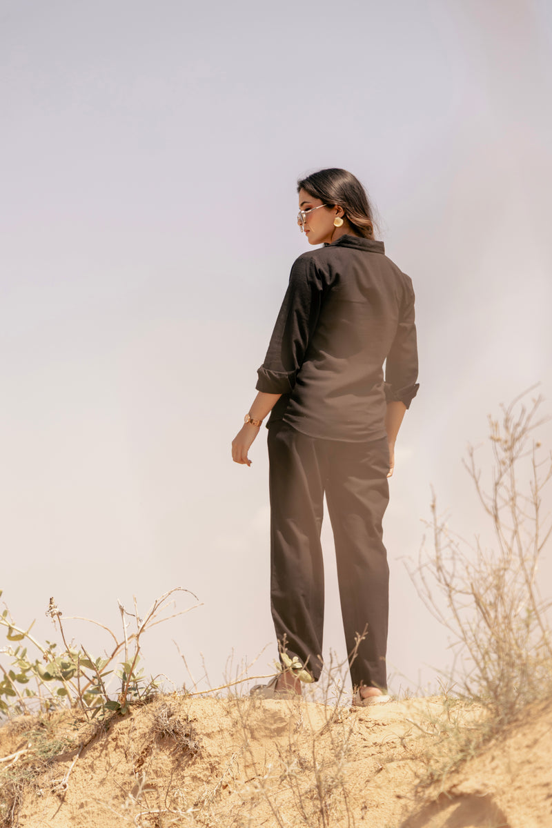 Person wearing a brown outfit standing on a sandy hill with a clear sky.