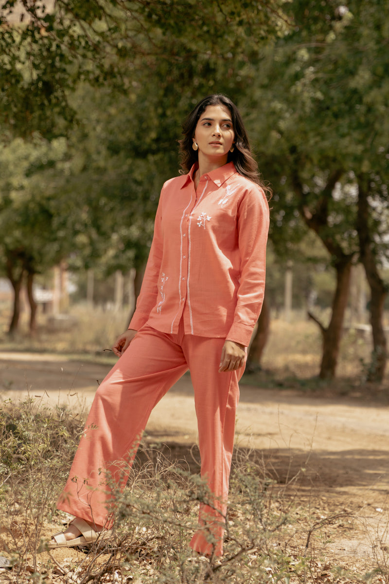 Woman in a peach outfit standing outdoors with trees in the background