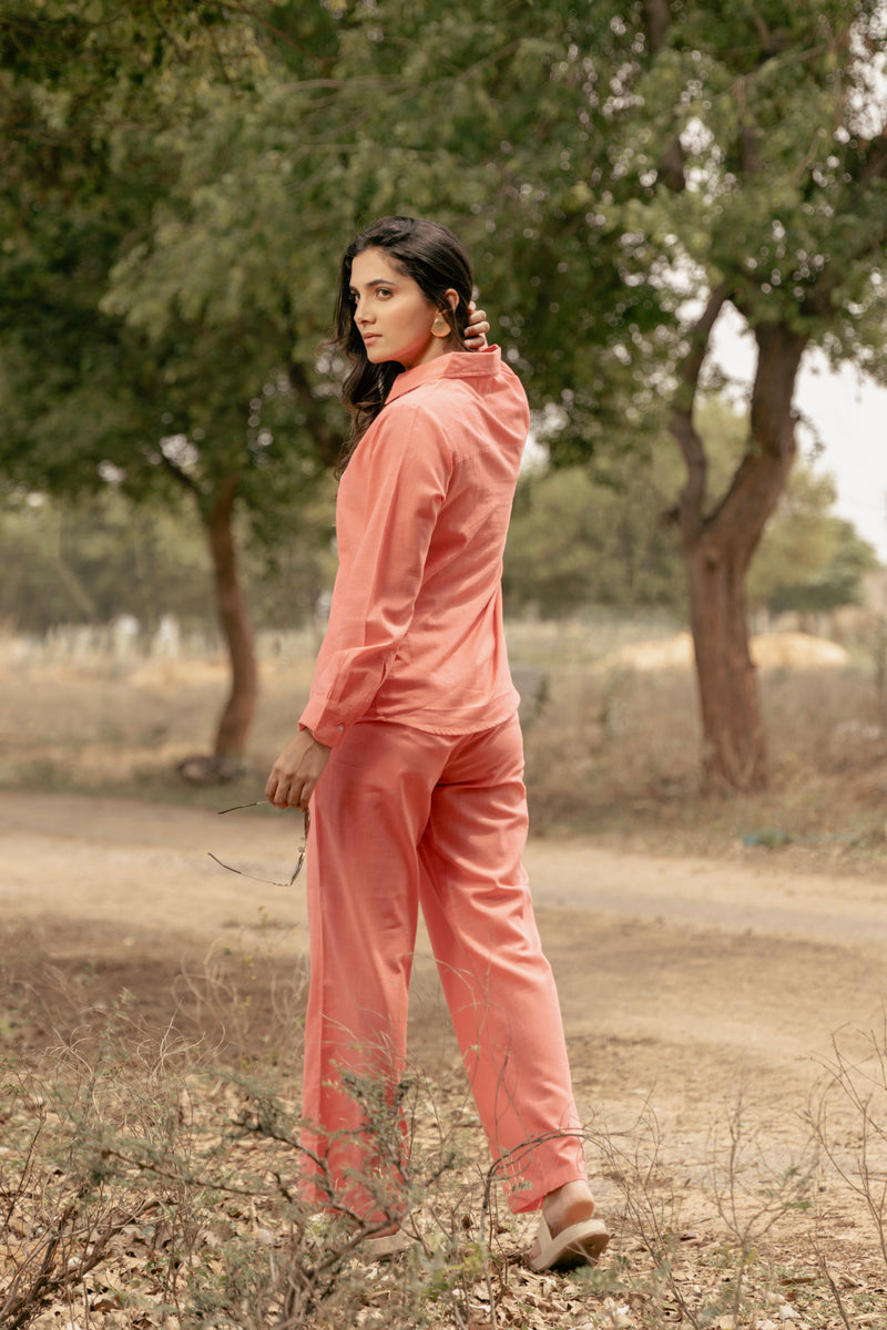 Woman in a peach tracksuit standing in a natural setting with trees and dry ground.