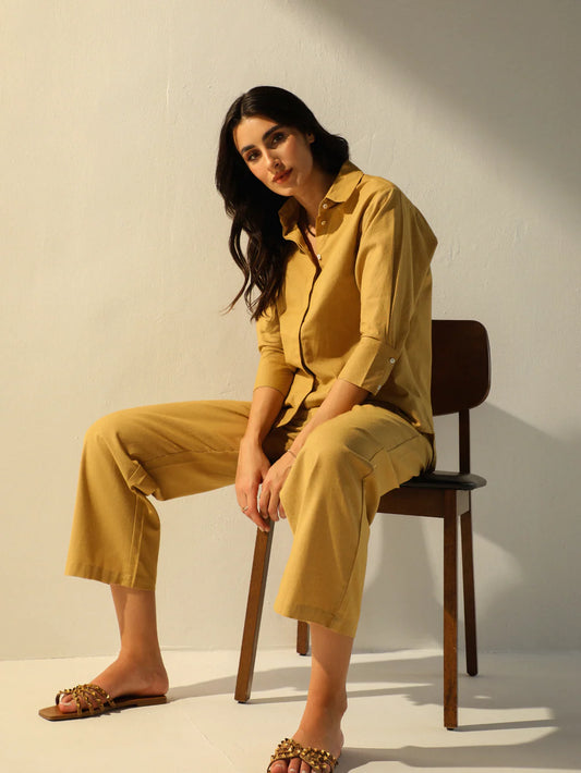 Woman in a mustard yellow outfit sitting on a wooden chair against a white background