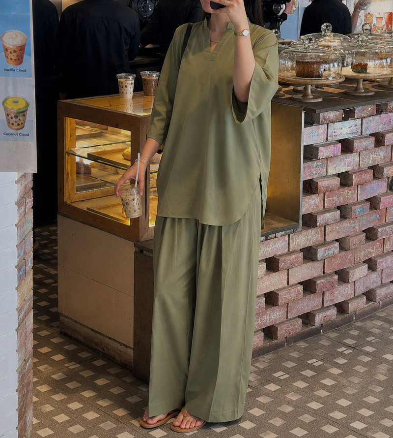 Person in a green outfit standing in front of a bakery counter with pastries.