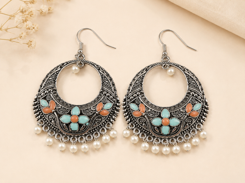 Ornate earrings with floral designs and pearl accents on a beige background