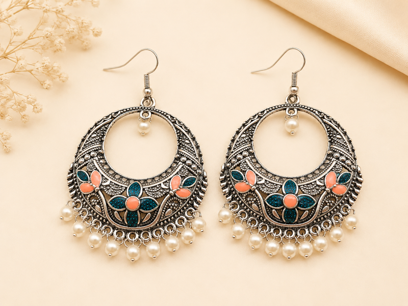 Ornate earrings with floral designs and pearl-like beads on a beige background