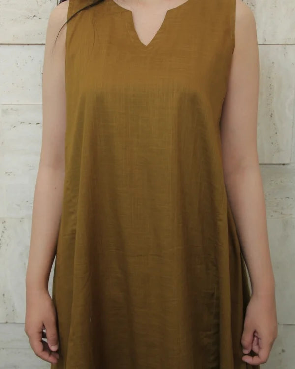 Person wearing a mustard yellow sleeveless dress against a light wooden panel background