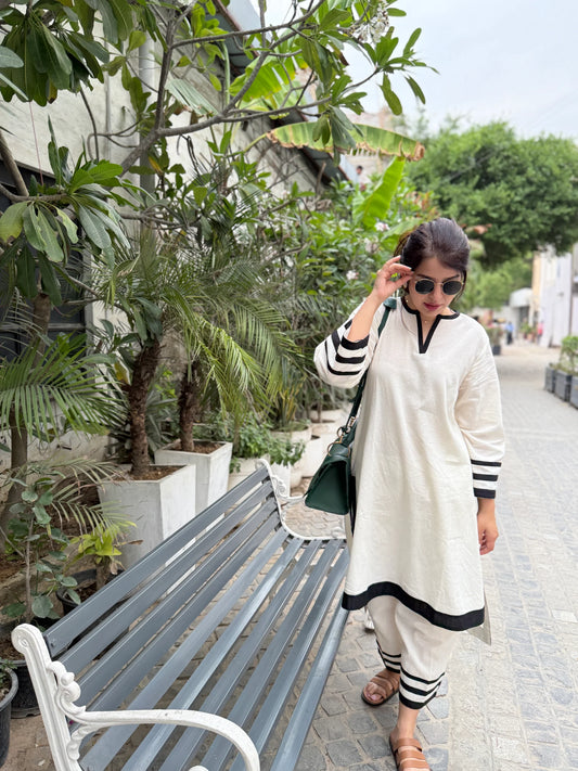 Woman in a white outfit with black accents walking in an urban garden setting.