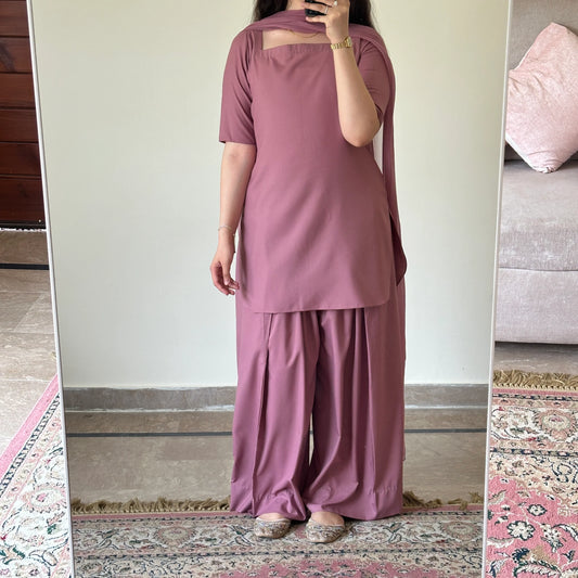 Person wearing a mauve outfit standing in front of a mirror.