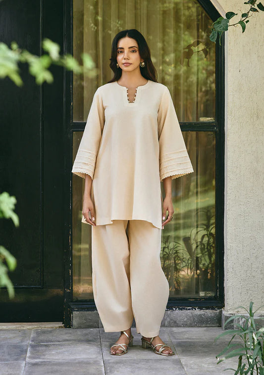 Woman wearing a beige outfit standing in front of a glass door with plants around.