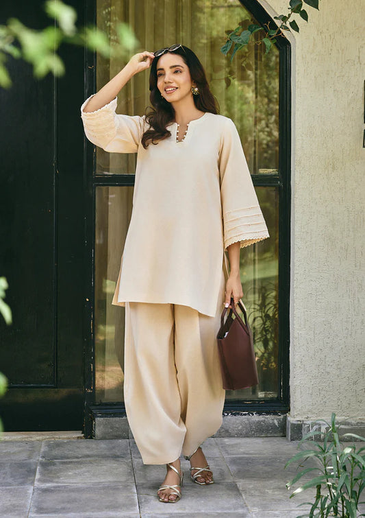 Woman in a beige outfit standing outside a building with greenery.