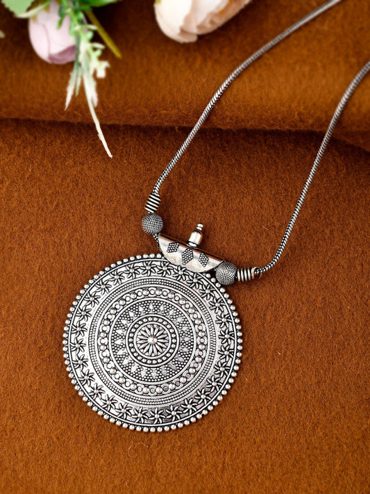 Silver necklace with a round, intricately designed pendant on a brown fabric background.