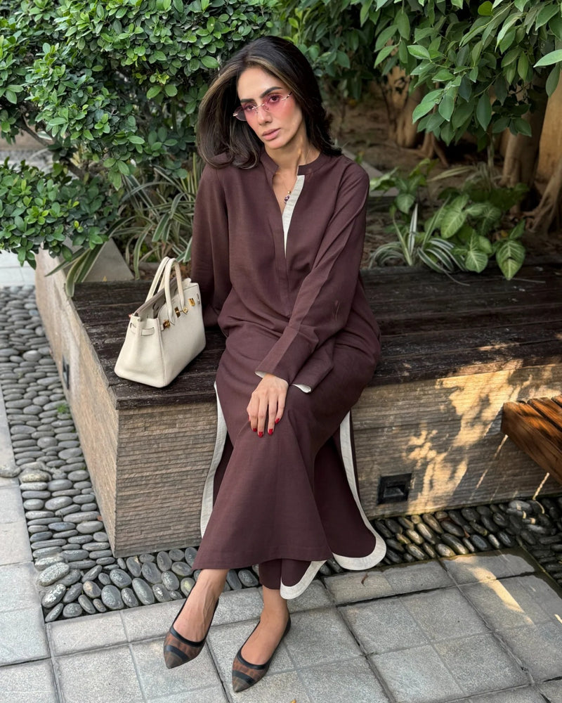 Woman in a brown outfit sitting on a wooden bench with greenery in the background