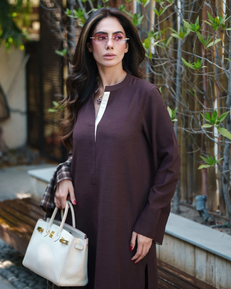 Woman in a brown dress holding a white handbag outdoors