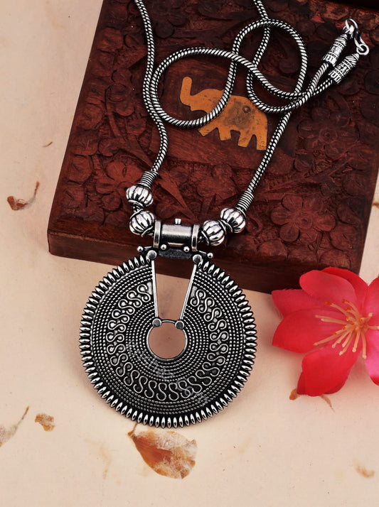 Silver necklace with a large circular pendant on a textured surface with a red flower.