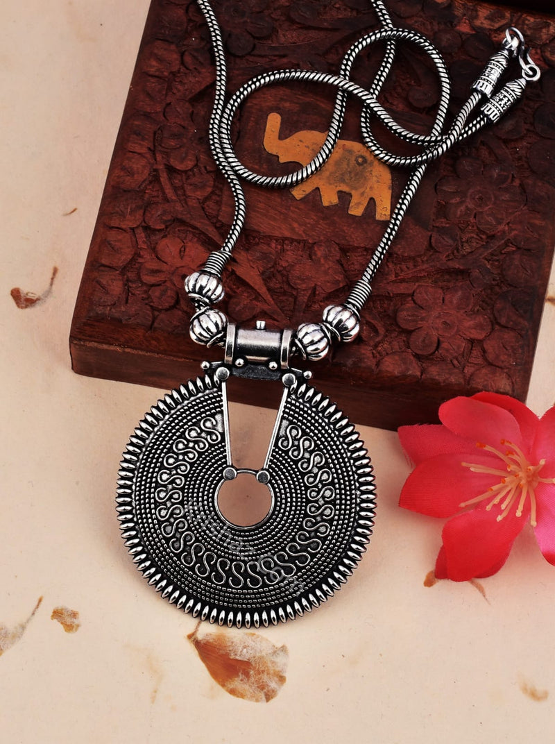 Silver necklace with a large circular pendant on a textured surface with a red flower.