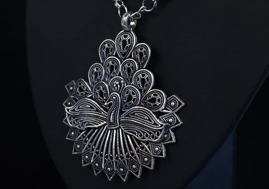Silver peacock-shaped pendant on a black background