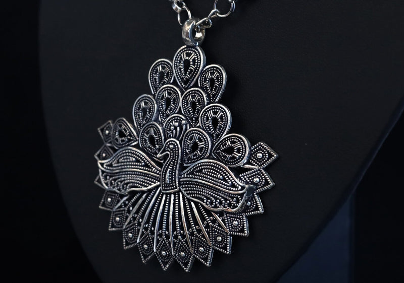 Silver peacock-shaped pendant on a black background