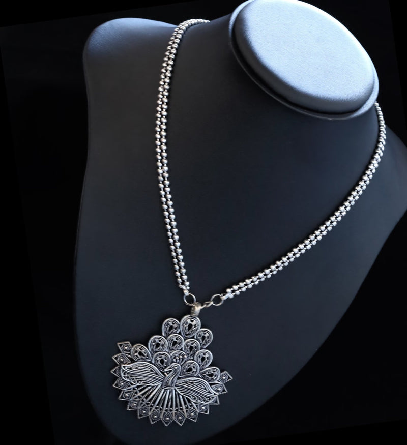 Silver necklace with a detailed pendant on a black mannequin bust.