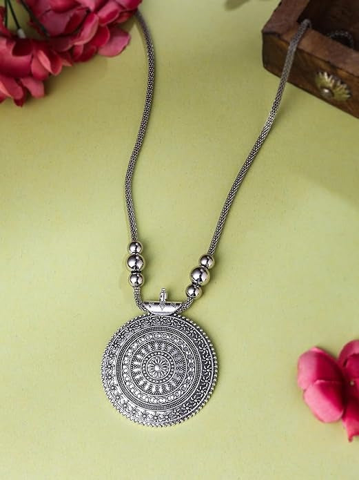 Silver necklace with decorative pendant on a green surface with pink flowers