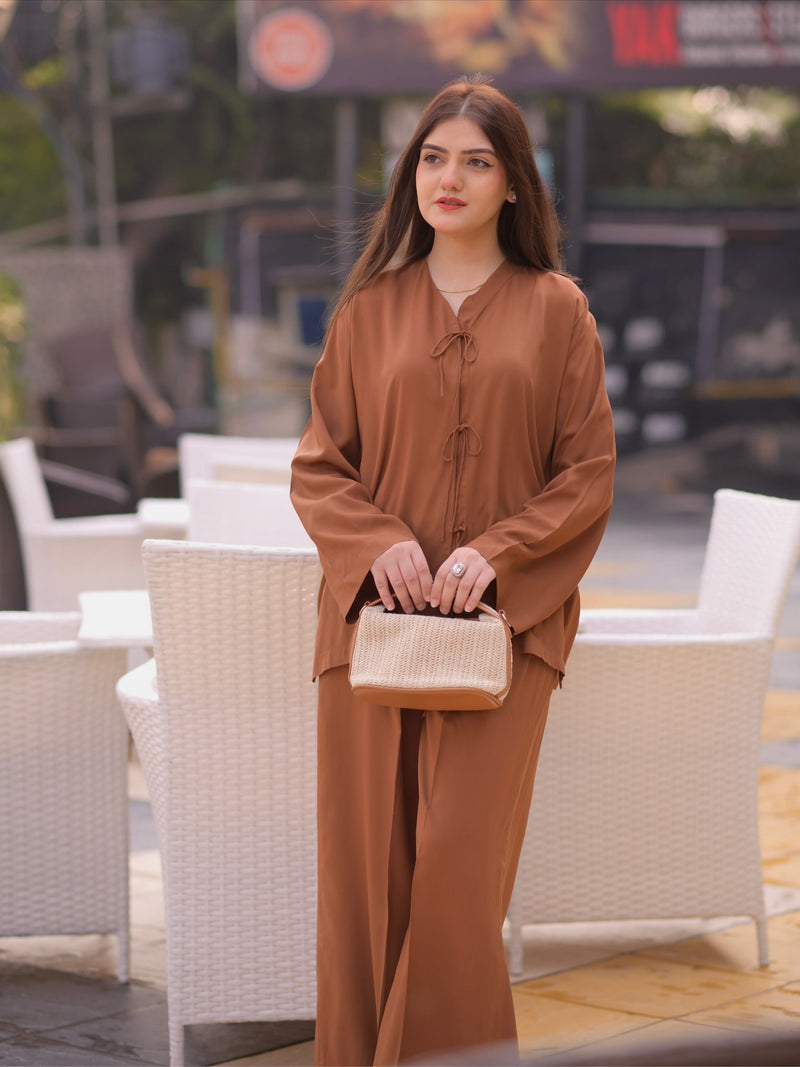 Woman in a brown outfit holding a beige handbag in an outdoor setting.