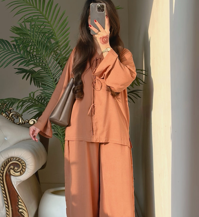 Person wearing a brown outfit taking a mirror selfie with a plant in the background